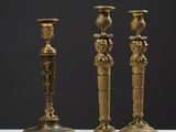 trois bougeoirs en laiton vieilli posés sur une table blanche, sur fond noir