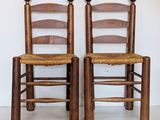 pair of wooden chairs with wicker seats against a white wall