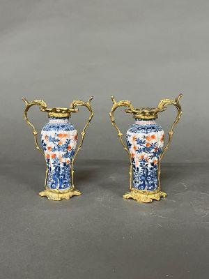 paire de vases bleus et blancs avec des anses dorées sur un fond gris