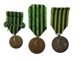 three medals are shown on a white background with a green and black stripe