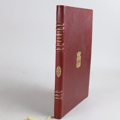 un livre rouge avec des bordures dorées posé sur une surface blanche
