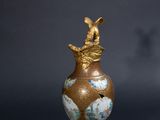un vase ancien orné d'un oiseau, à côté d'un bouchon