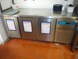 trois réfrigérateurs en acier inoxydable dans une cuisine au sol carrelé de couleur orange