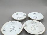 quatre assiettes blanches ornées de motifs floraux, posées sur un fond gris
