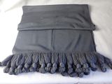 a black scarf with tassels on it on a bed
