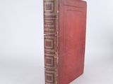 an old book with a red cover sitting on top of a white surface