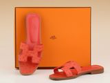 une paire de sandales roses et une boîte orange posée sur une surface blanche