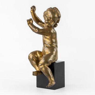 une statue en bronze représentant un enfant assis sur un bloc