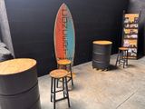 a surfboard sitting on top of a wooden stool next to a stack of barrels