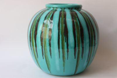 un vase bleu orné de rayures vertes, posé sur un fond blanc
