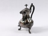 a silver coffee pot on a stand with a handle