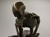 a bronze statue of a skeleton sitting on a rock