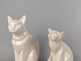une paire de figurines de chats en céramique blanche posées sur une surface grise