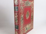 an old book with a red cover and gold trim