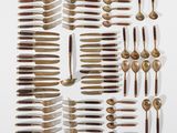 Plusieurs cuillères et fourchettes sont disposées sur une surface blanche
