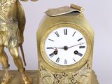 a gold clock with a statue of a man holding a sword