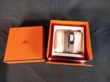 une boîte orange contenant une montre, posée sur une surface noire