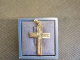 pendentif en forme de croix plaqué or, présenté dans un coffret bleu sur fond gris