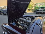 a black car with a hood open and a green truck in the background