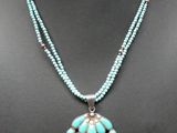 un collier composé de perles de turquoise et d'un pendentif en argent, présenté sur un mannequin