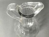 a clear glass pitcher with a black handle on a table