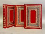 three red books with gold trims are sitting on a white surface