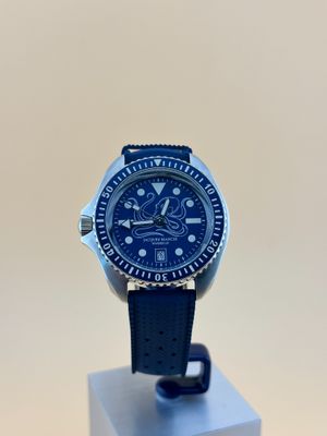 une photo d'une montre posée sur un socle, sur une surface blanche
