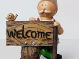 statue of a gnome holding a welcome sign with a bird perched on top of it