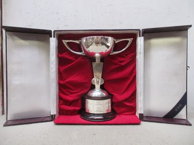 un trophée en argent dans un coffret rouge posé sur un tissu rouge
