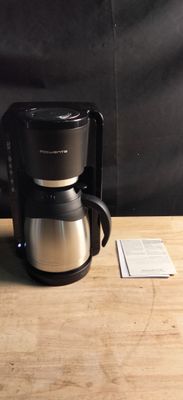une cafetière posée sur une table en bois, à côté d'une tasse de café