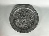 une plaque d'argent ornée d'un motif sur une surface blanche