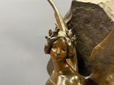 une statue en bronze représentant une femme ailée, perchée sur un rocher