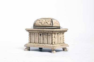 une vieille boîte en bois, dont le couvercle est orné de sculptures, posée sur une surface blanche