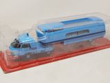 un petit train jouet bleu dans une boîte transparente, posé sur une surface blanche