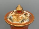 a red vase with a gold lid sitting on a table