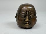 une petite sculpture en bronze représentant un visage sur une surface blanche