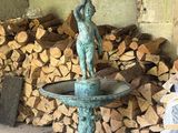une statue représentant un garçon, située sur une fontaine devant un tas de bois de chauffage