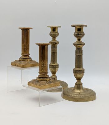 trois bougeoirs en laiton posés sur des socles en acrylique transparent, sur fond blanc