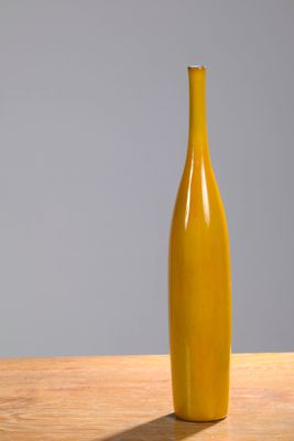 a yellow vase sitting on top of a wooden table next to a gray wall