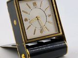 une horloge noire et dorée posée sur un socle, sur une surface blanche
