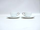two white cups and saucers sitting on top of a white table