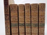 six old books lined up in a row on a white surface