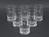 six verres à shot transparents ornés de flocons de neige, posés sur une surface noire