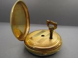 a gold pocket watch with a key inside of it