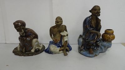 three figurines of people sitting on a white surface, one of them is holding a pot and the other is holding a bowl
