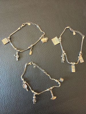 three silver bracelets with charms and charms on them on a black surface