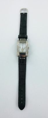 une photo d'une montre posée sur une surface blanche, avec un bracelet noir