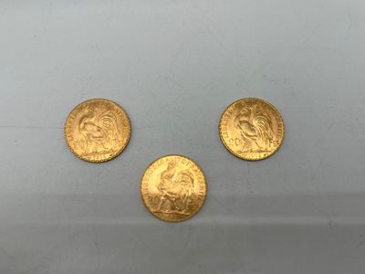 On voit trois pièces d'or sur une surface blanche