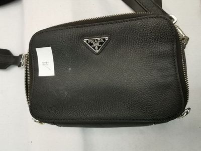un sac à main noir orné d'un logo triangulaire, posé sur une surface blanche
