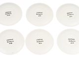 six white plates with black writing on them sitting on a white surface